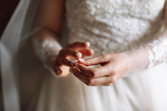 cropped photo of gentle hands of the bride standing in a white lace dress puts a wedding ring on her