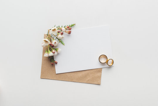 top view of empty card with brown craft paper envelope and wedding rings on grey background